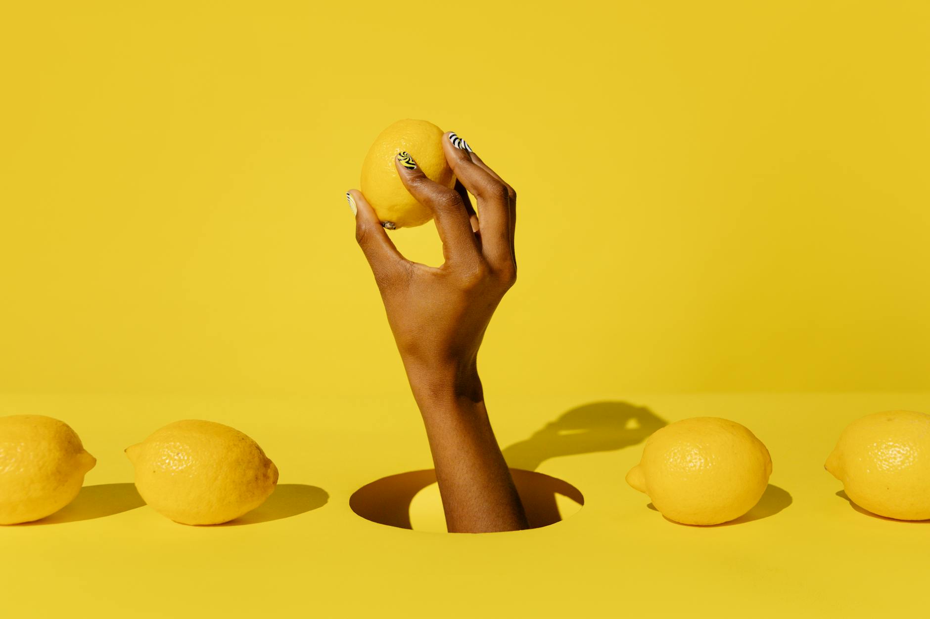 Hand holding a fresh lemon against a bright yellow background, symbolizing renewal and gentle sensuality