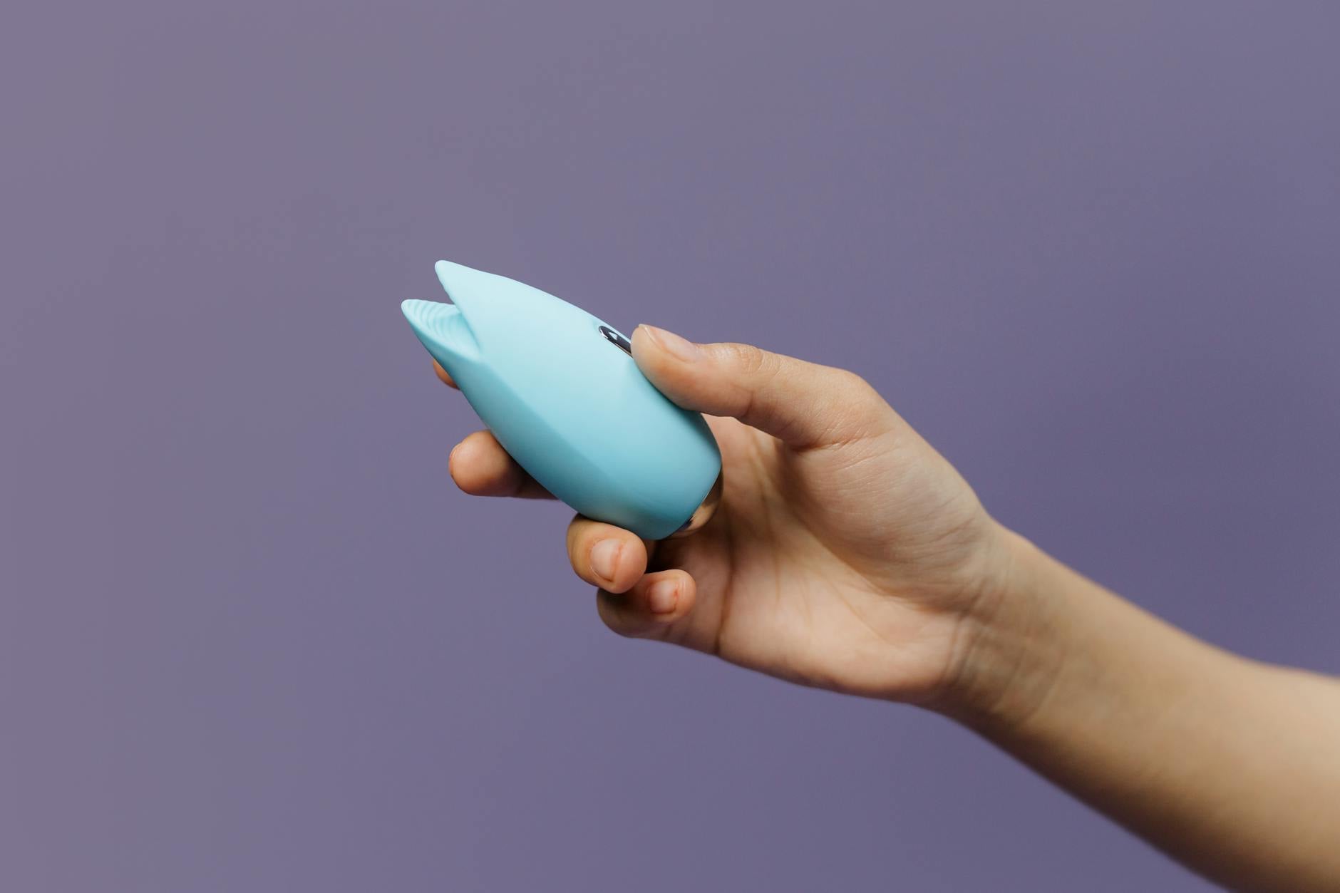 Hand holding a blue lemon vibrator against a purple background, representing sensual pleasure and touch exploration