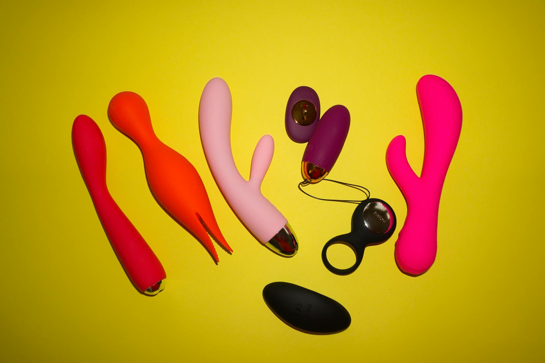 Colorful adult toys arranged on bright yellow background, including vibrators and pleasure devices