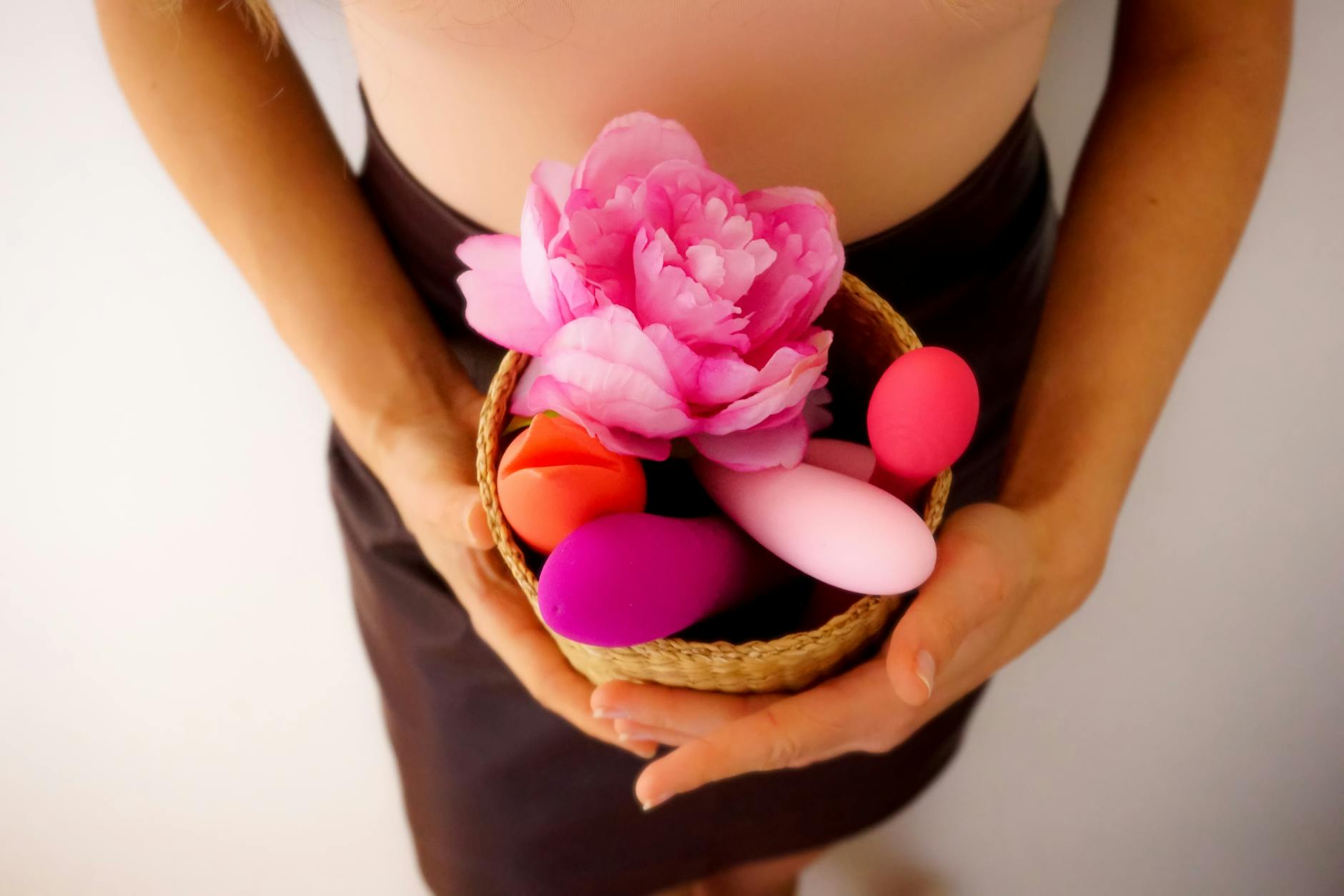 Hands holding colorful clitoral vibrators and intimacy toys in a basket